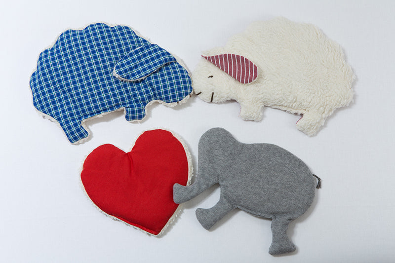 Das Bild zeigt alle Plüsch-Wärmekissen-Varianten von Kissentraum: blau kariertes Schaf, rot-kariertes Schaf, rotes Herz, grauer Elefant. 